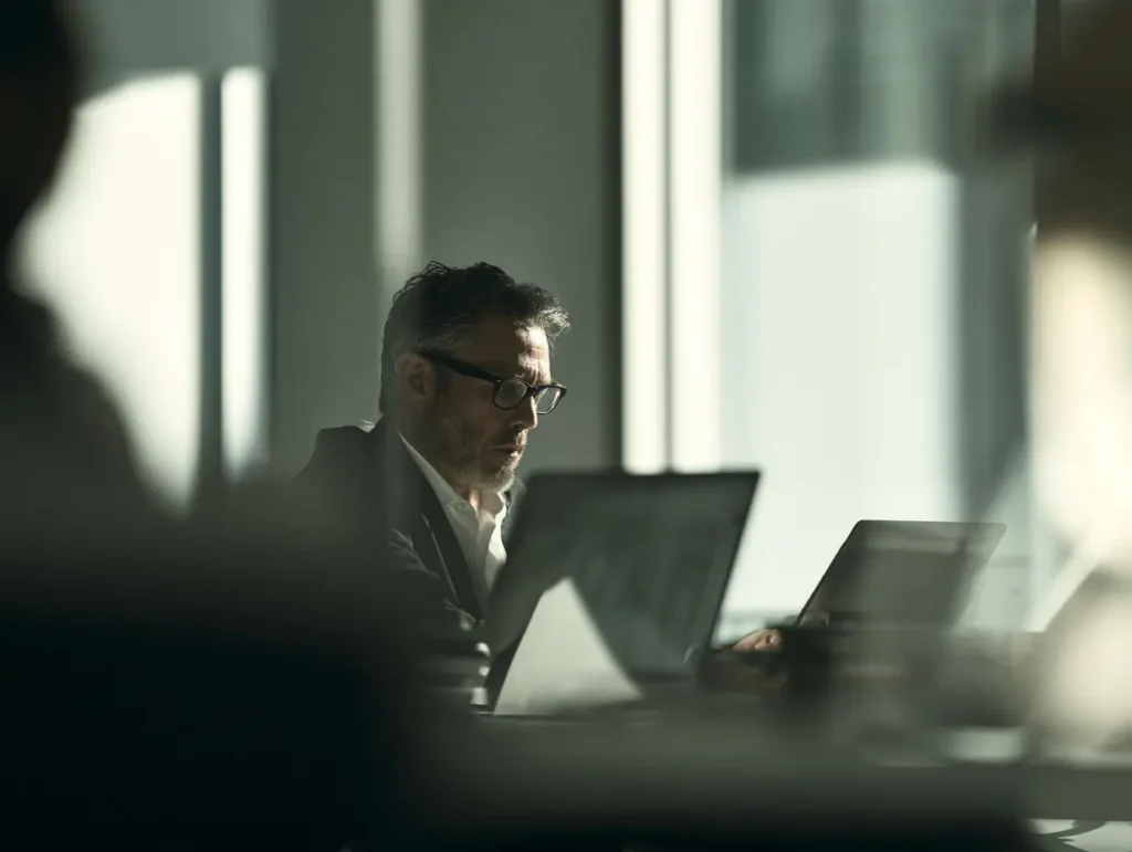 Mann im Büro prüft Daten auf zwei Laptops